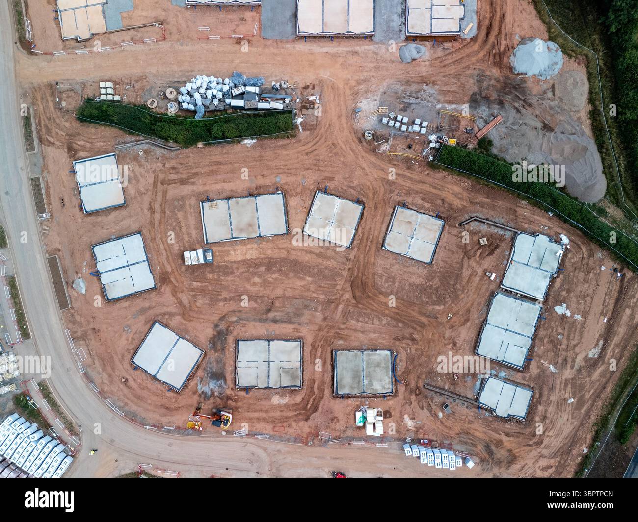 Vista aerea di un cantiere che mostra le fondamenta in calcestruzzo per nuove case, materiali da costruzione e attrezzature per il movimento terra Foto Stock