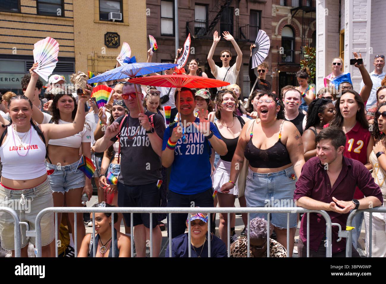 Una folla vivace a una parata del Pride, molti con bandiere arcobaleno e tifosi. Persone di diversa provenienza ed età sorridono e festeggiano. Due uomini dentro Foto Stock