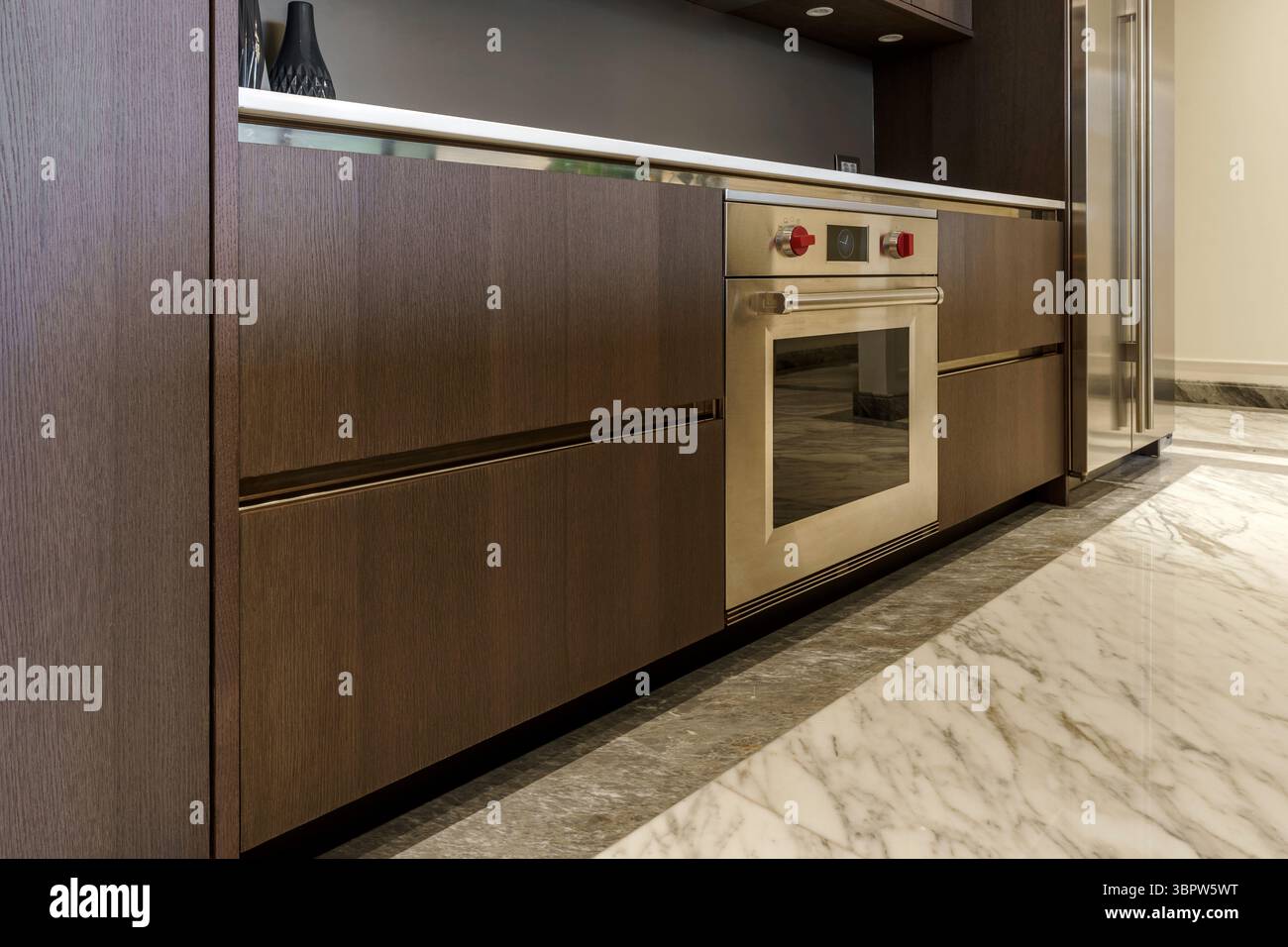 Forno Wolf in acciaio inox installato sotto un ripiano bianco con cassetti in legno scuro. Lussuosa cucina con pavimento in marmo. Foto Stock