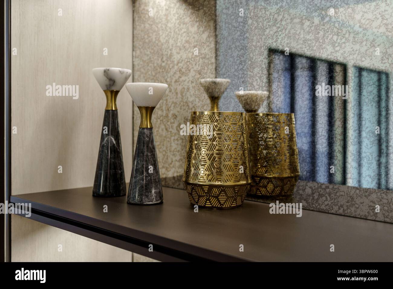 Elegante arredamento con portacandele in marmo e un vaso con motivi dorati su uno scaffale scuro. Interni lussuosi con dettagli di design su uno specchio testurizzato Foto Stock