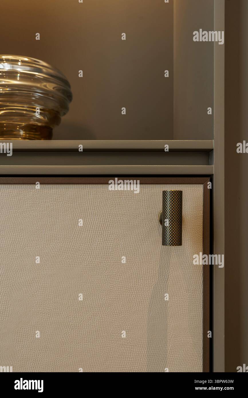 Primo piano di una moderna maniglia in ottone testurizzato su una porta dell'armadio con pannelli in pelle beige. Arredi di lusso in un design contemporaneo. Foto Stock