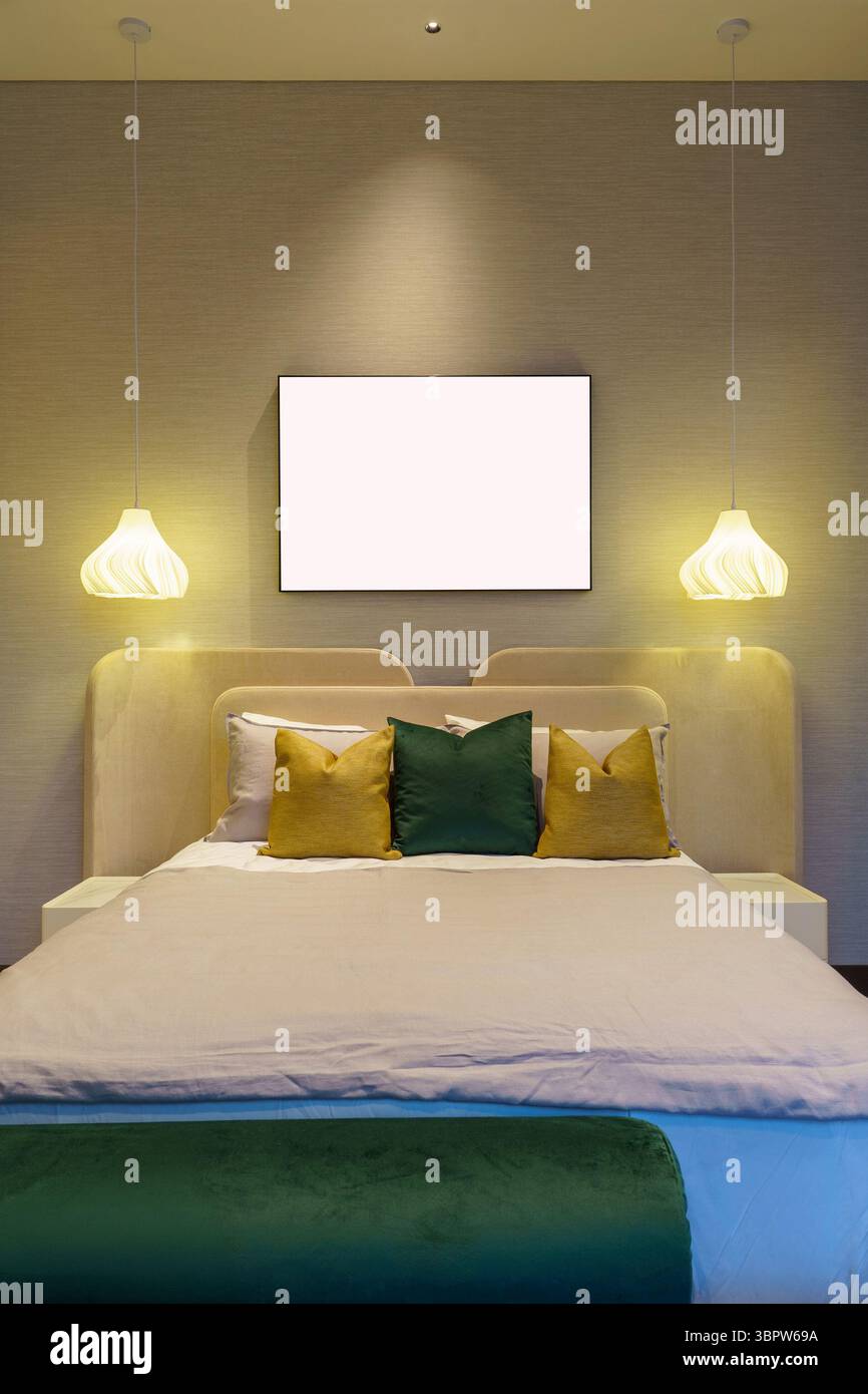 Vista simmetrica di una camera da letto moderna con una grande cornice vuota per il mockup. Le due luci a sospensione sono appese su un letto ben fatto con cuscini verdi e gialli Foto Stock