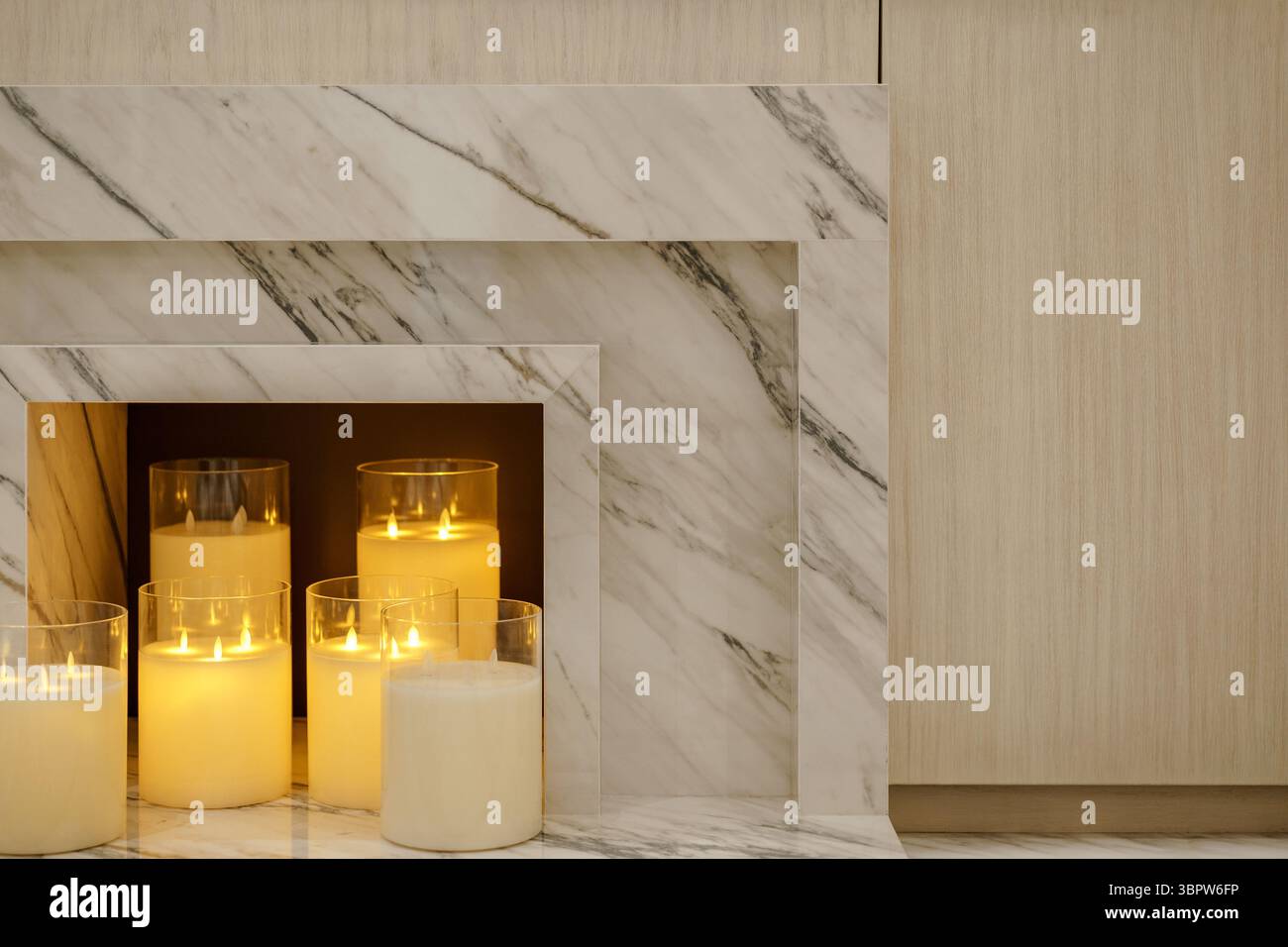 Primo piano di un moderno caminetto in marmo con candele elettriche. La combinazione di marmo venato e legno chiaro crea un ambiente intimo e lussuoso Foto Stock