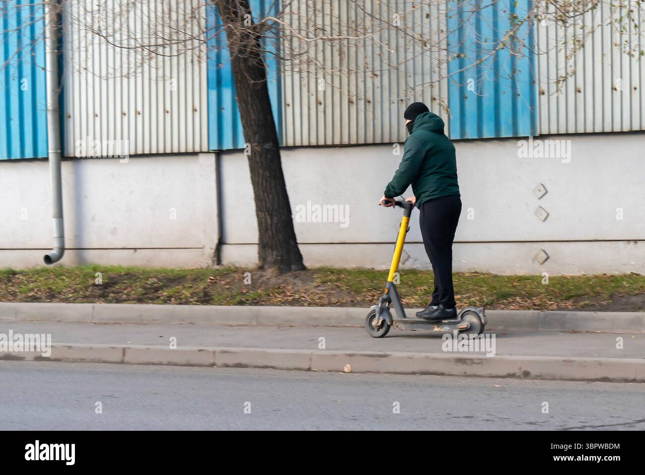 Un uomo con abiti autunnali guida uno scooter elettrico sul marciapiede. Movimento mobile dei cittadini in città. Foto Stock