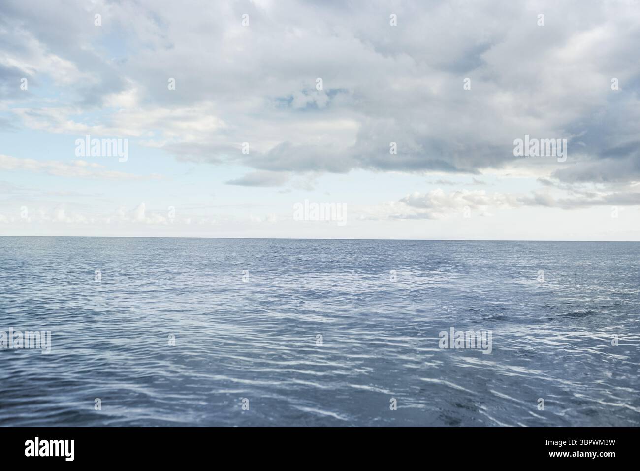 Design piatto l'oceano calmo viene mostrato raggiungendo l'orizzonte lontano sotto un cielo parzialmente nuvoloso con increspature Foto Stock