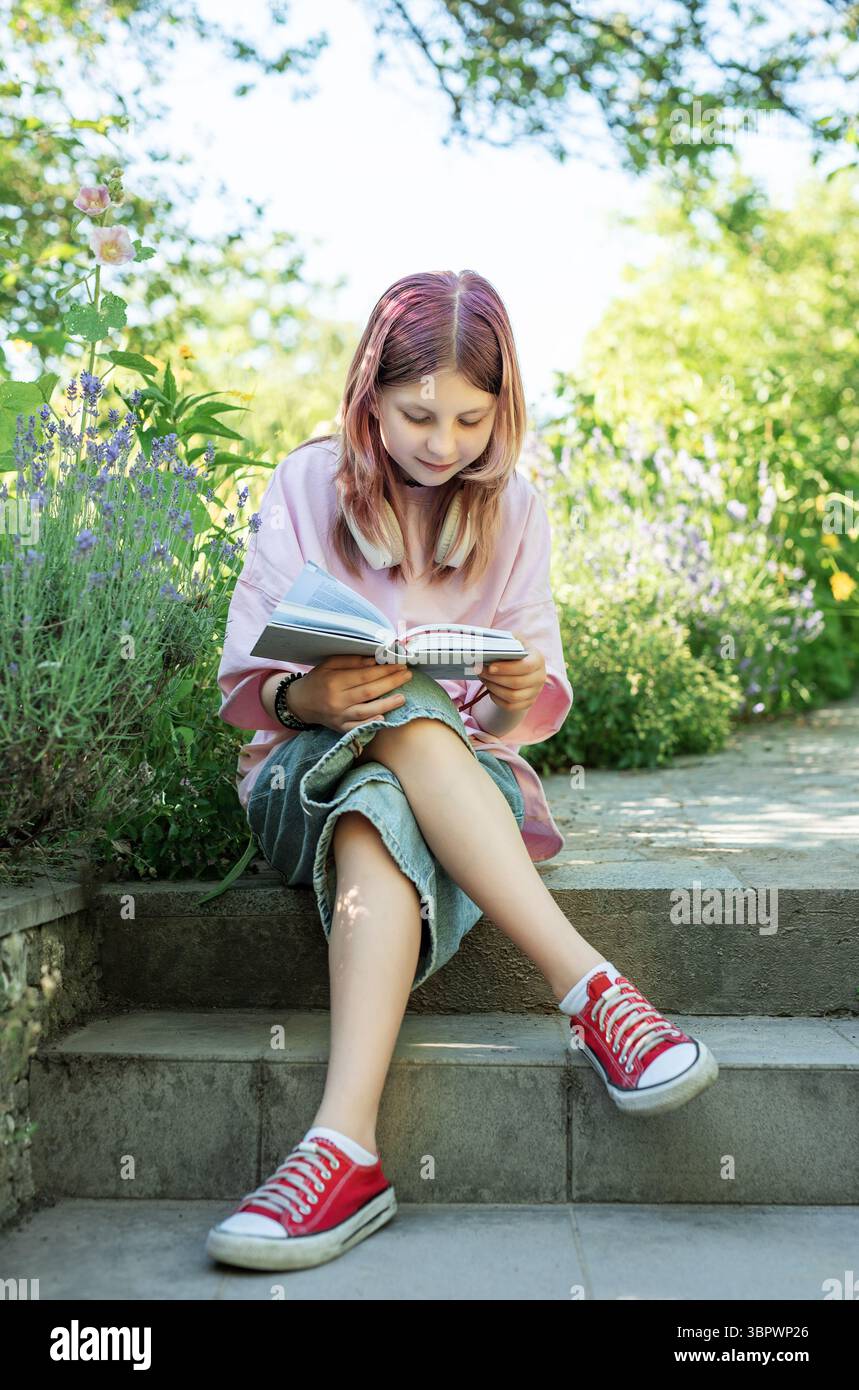 Ragazza che si diverte a leggere in un tranquillo giardino, trovando conforto e conoscenza nella letteratura Foto Stock