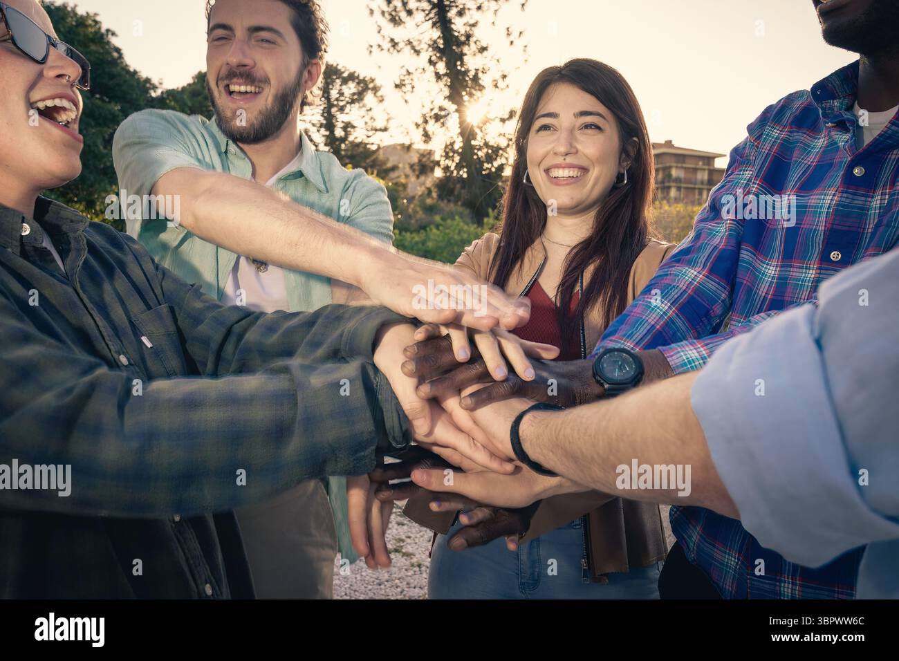 Primo piano di un gruppo eterogeneo di amici che stringono le mani al centro, simboleggiando il lavoro di squadra, l'unità, il sostegno e un collaboratore di successo Foto Stock
