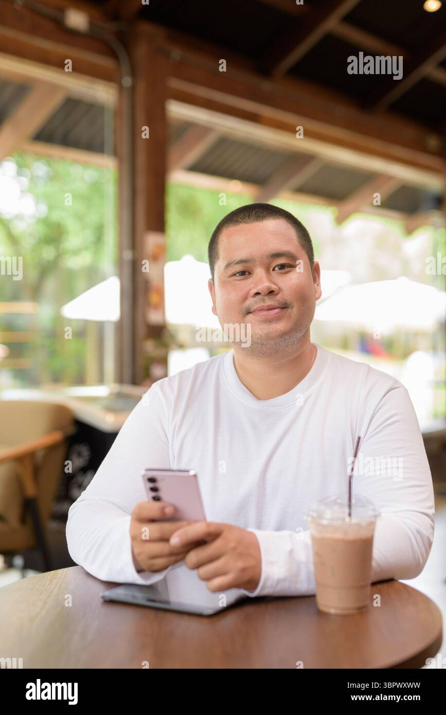Giovane asiatico più grande uomo felice seduto in un bar ristorante Foto Stock