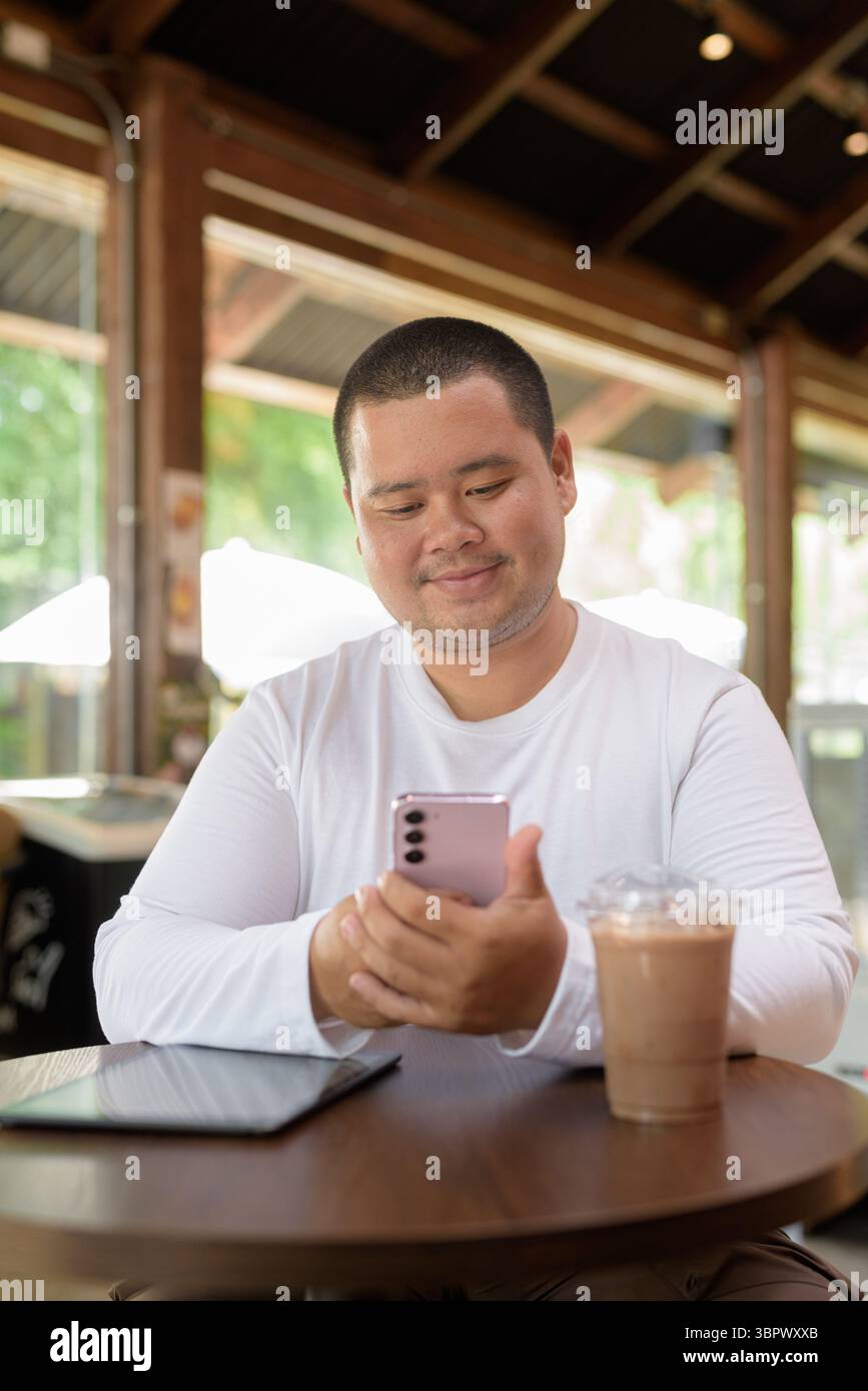 Giovane asiatico più grande uomo felice seduto in un bar ristorante Foto Stock