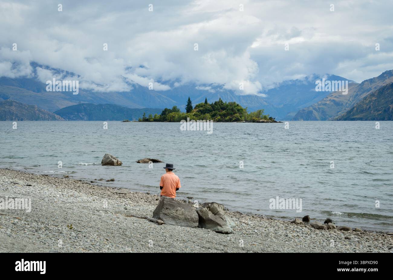 Uomo seduto sulla roccia e godendo della vista di Ruby Island. Lago Wanaka. Regione di Otago. Isola del Sud. Foto Stock