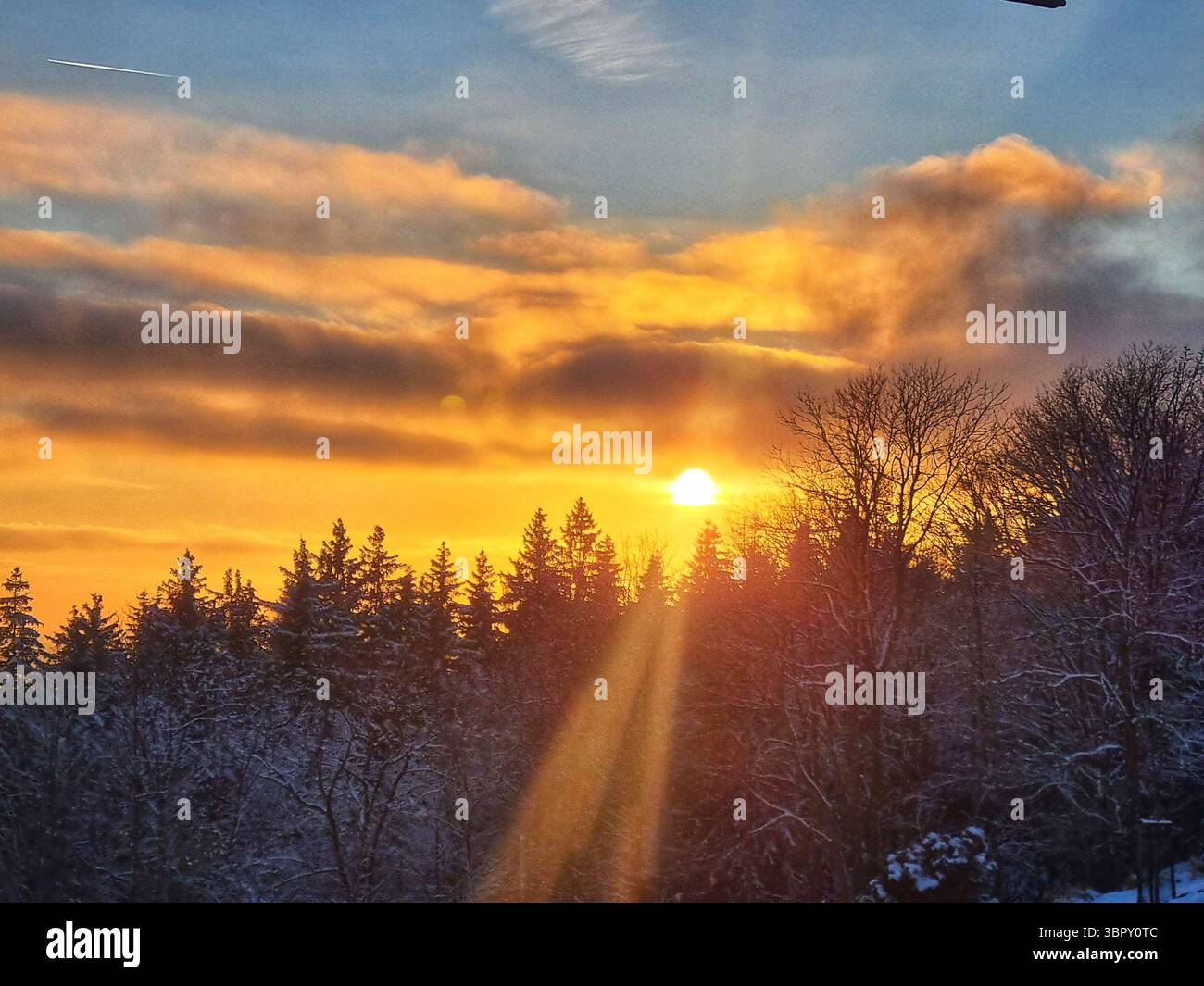 I bellissimi raggi del sole e il bagliore delle lenti esplodono da dietro una collina dalla silhouette sagomata, creando una scena stimolante e stimolante durante un tramonto invernale - Immagine stock catturata con smartphone