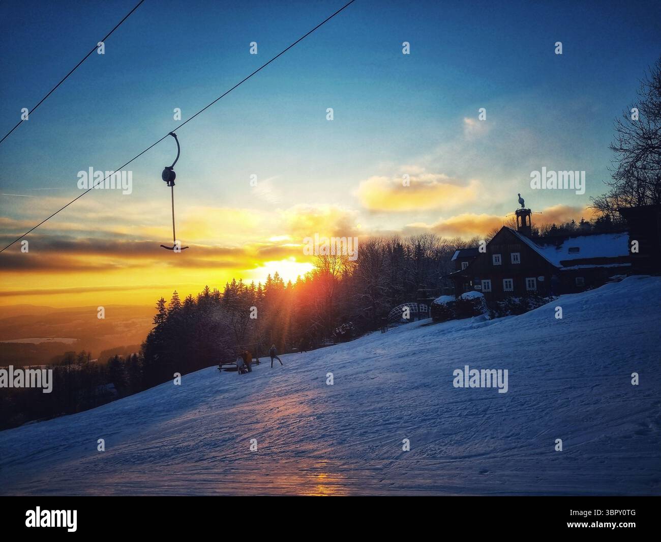 Un'ampia e panoramica vista di una pista da sci innevata in una località montana ceca durante un bellissimo e tranquillo tramonto invernale, con nuvole colorate all'orizzonte. - Immagine stock catturata con smartphone