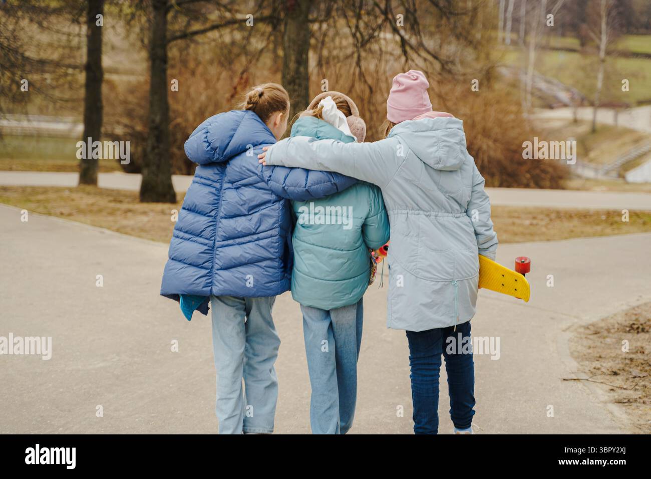 Le ragazze camminano insieme, abbracciano le spalle, ognuna con uno skateboard. Giacche, jeans e sneaker sfoggiano lo Street style invernale. Amicizia all'aria aperta, moventi Foto Stock