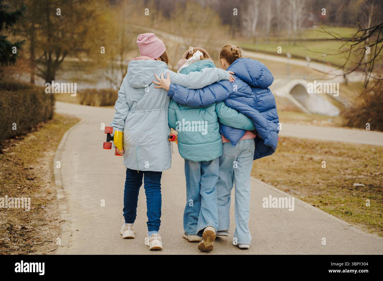 Le ragazze camminano insieme, abbracciano le spalle, ognuna con uno skateboard. Giacche, jeans e sneaker sfoggiano lo Street style invernale. Amicizia all'aria aperta, moventi Foto Stock