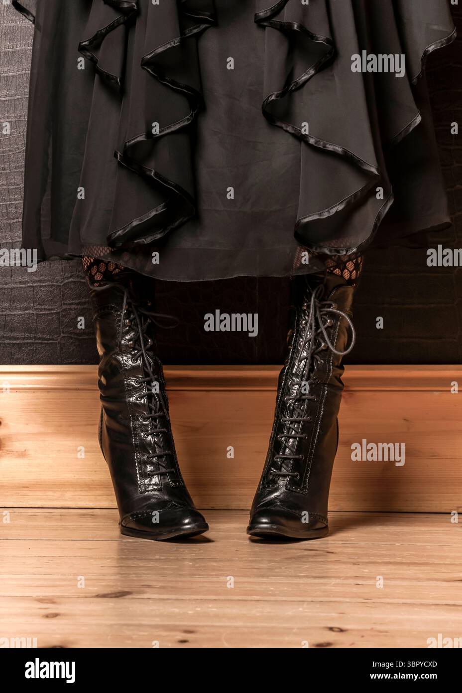 Una persona indossa stivali con lacci neri e un abito nero. Foto Stock