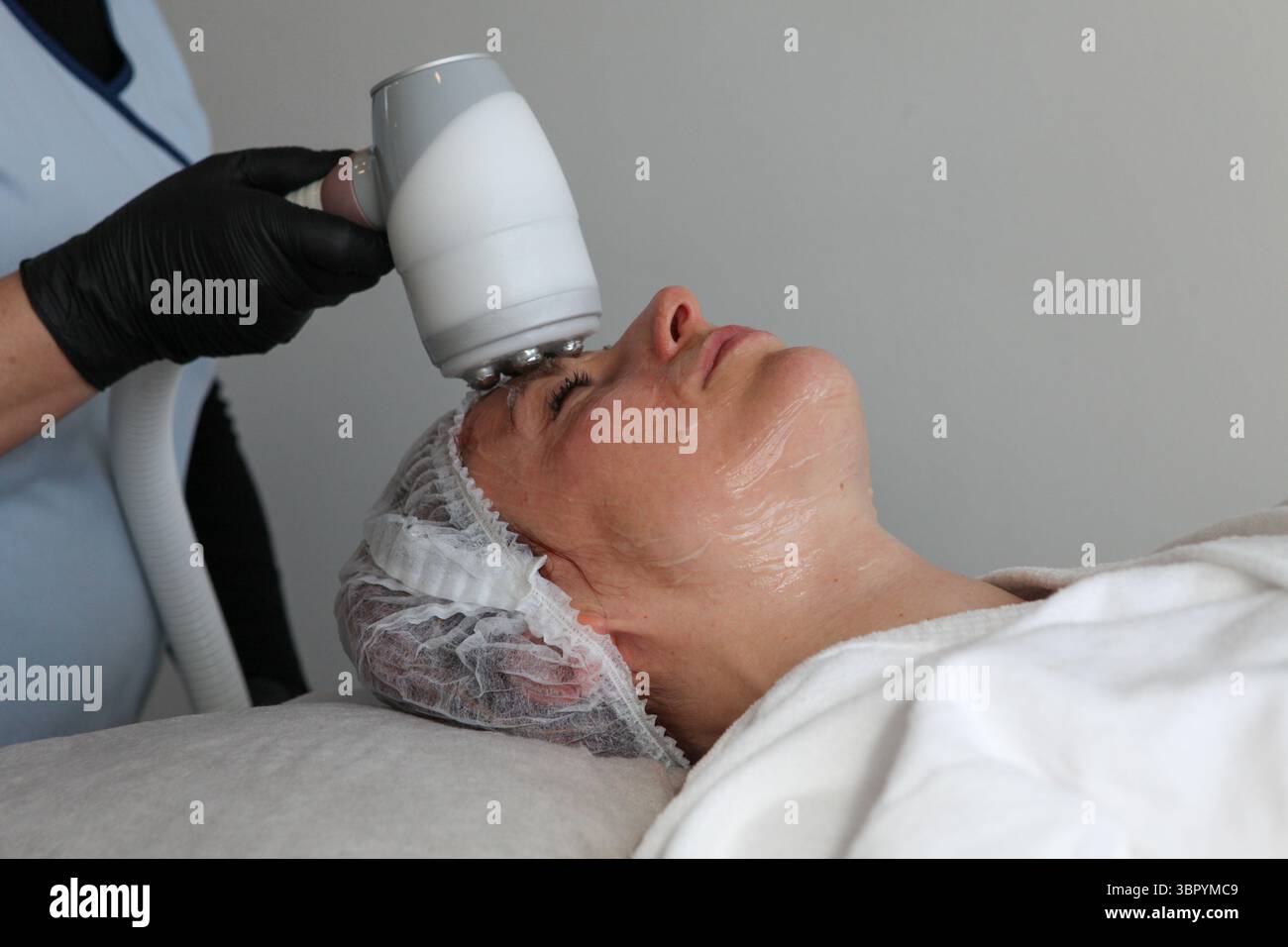 Giovane donna che riceve un trattamento viso Cryo-radio-frequenza presso una clinica di bellezza eseguita da uno specialista con attrezzature specializzate, concentrandosi sulla pelle Foto Stock