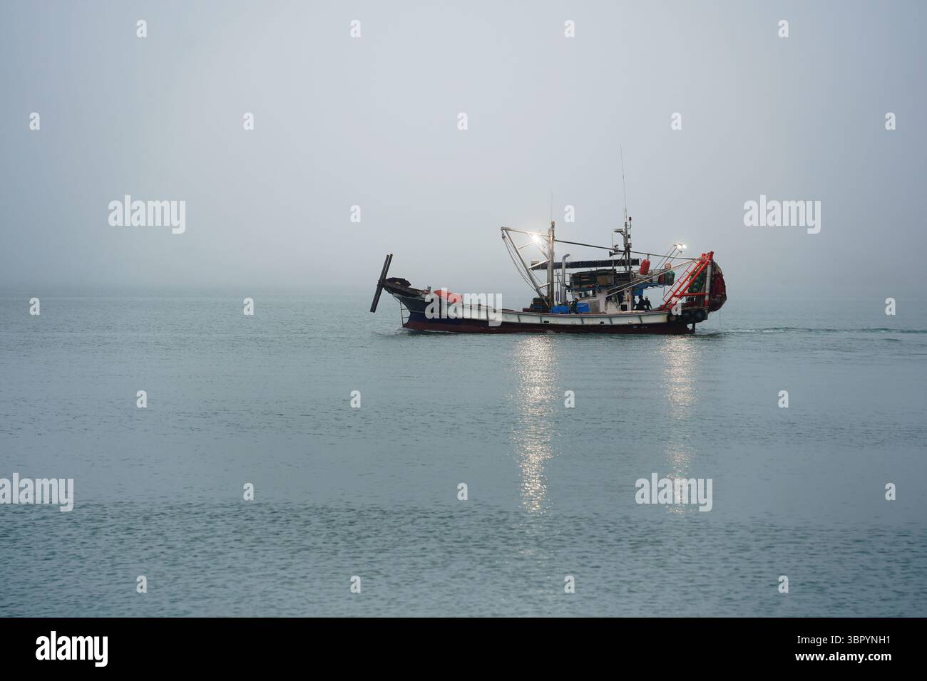 Barca da pesca a lume di acqua che galleggia sul mare con luci riflesse Foto Stock