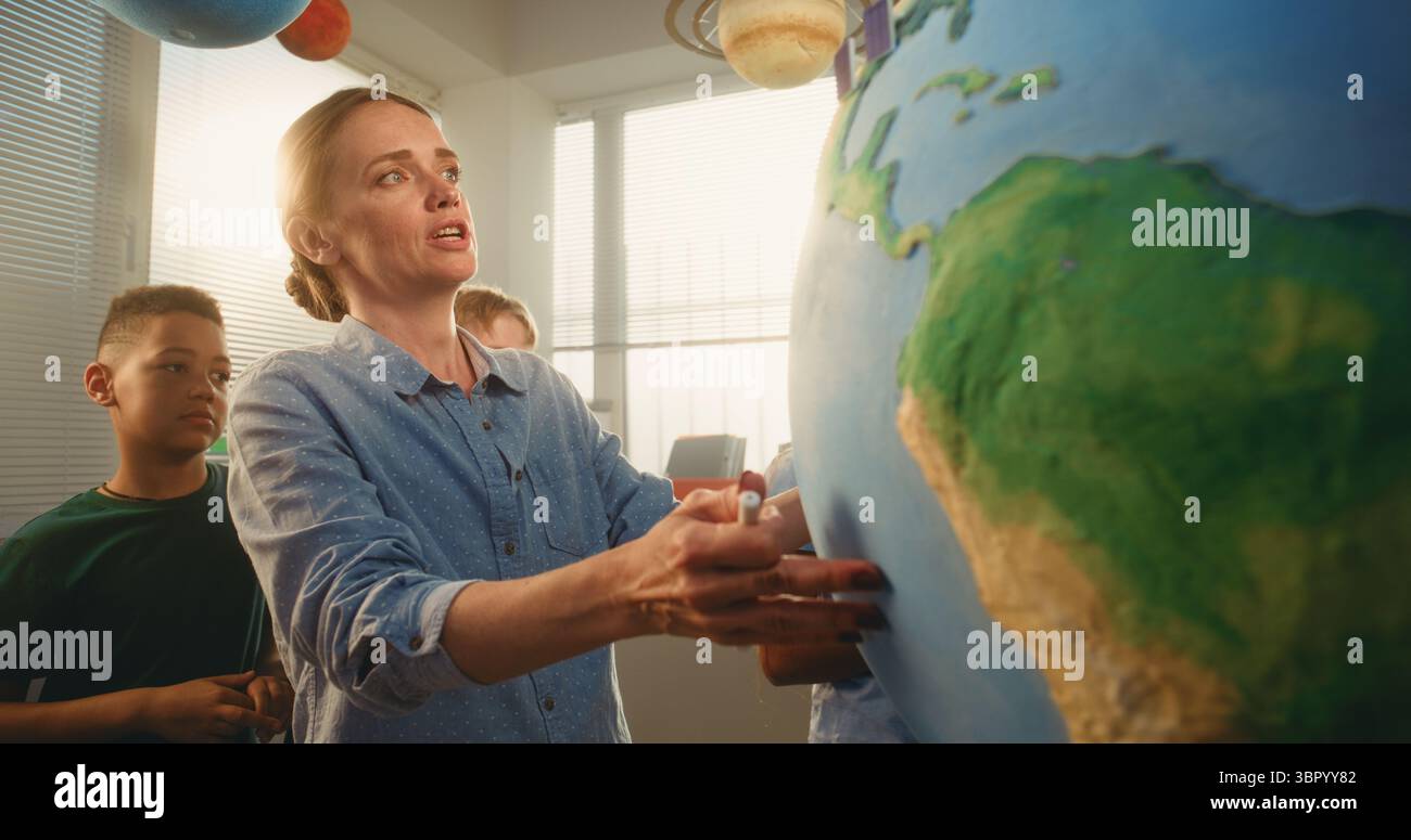 Classe STEM: Insegnante donna che spiega le energie rinnovabili al team di bambini intelligenti che utilizzano il modello Terra con modelli 3D di turbine eoliche e pannelli solari. Gli studenti delle scuole elementari imparano l'ecologia, la geografia. Foto Stock