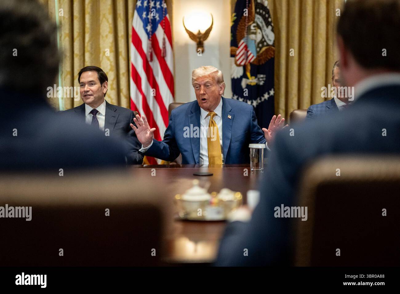 Il presidente Donald J. Trump parla durante una riunione di gabinetto, seduto accanto al Segretario di Stato Marco Rubio. L'incontro si svolge in un ambiente formale con bandiere statunitensi, tende dorate e sigillo presidenziale, con funzionari parzialmente visibili in primo piano. White House, Washington, D.C., l'8 luglio 2025. Per gentile concessione della Casa Bianca. Foto Stock