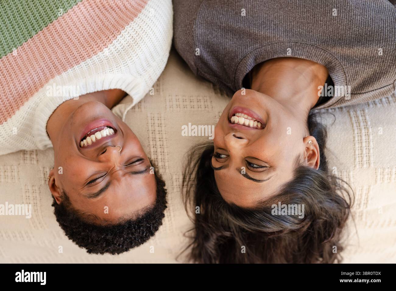 Coppie diverse che si trovano fianco a fianco su una coperta in tessuto color crema a casa e sorridono insieme. Romanticismo, relax, intimità, accogliente, connessione, amore, Foto Stock