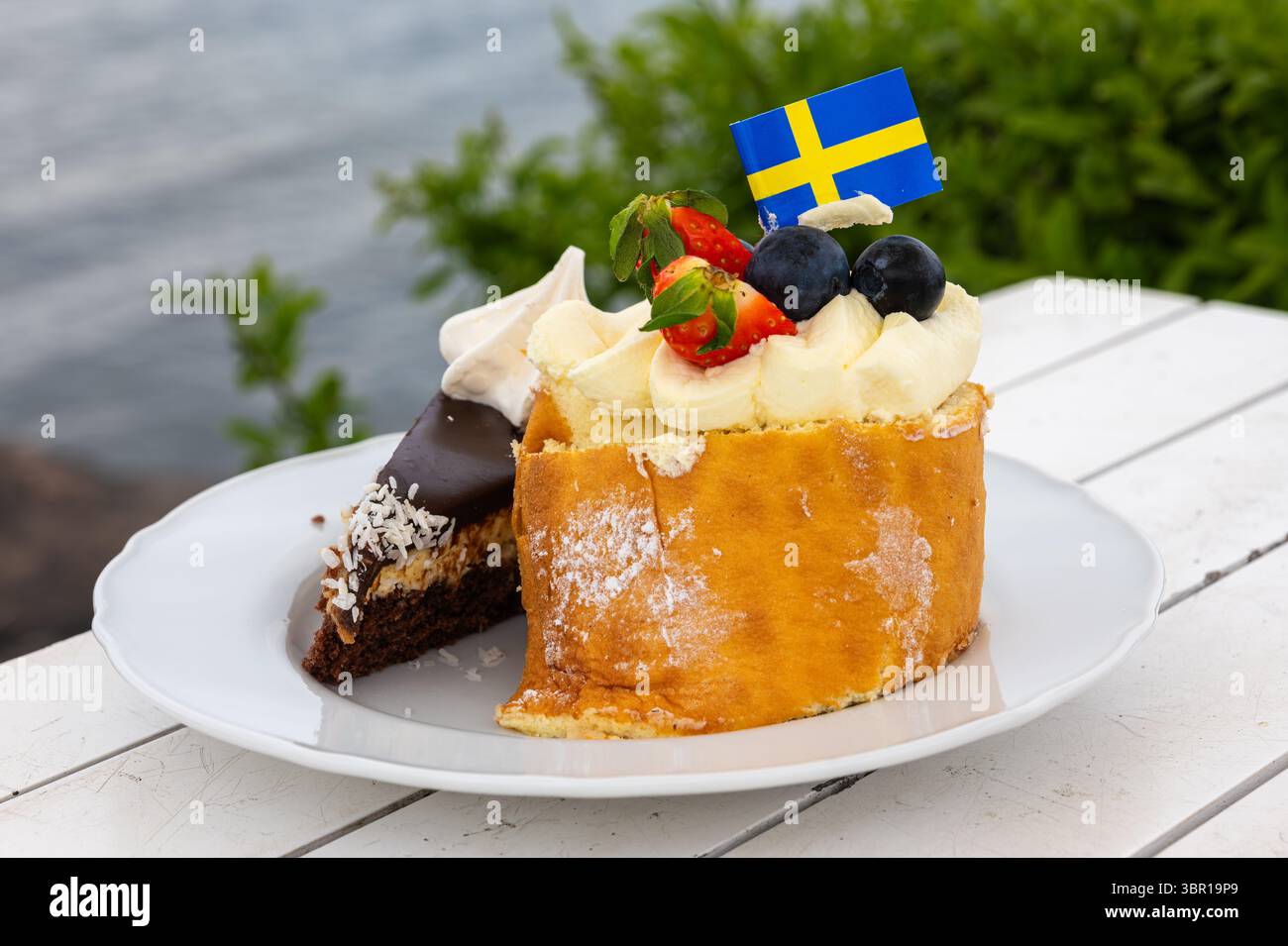 Un piatto con due tipi di torta, uno al cioccolato e uno alla crema, decorato con una bandiera svedese, adagiato su una vista panoramica sul lungomare dell'isola di Vaxholm, SW Foto Stock