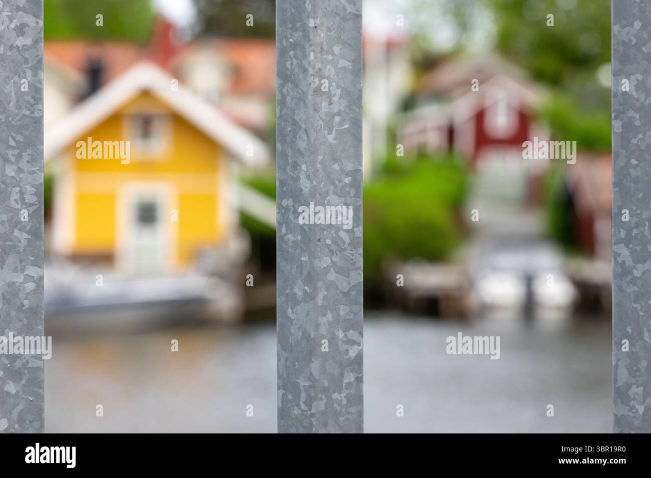 Una vista sfocata delle case colorate svedesi rosse e gialle sull'isola di Vaxholm dietro una recinzione metallica, con un tranquillo corso d'acqua in primo piano. Foto Stock