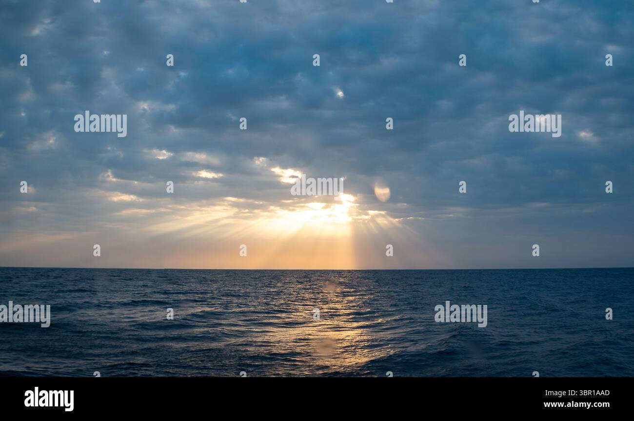 I delicati raggi del sole sbirciano attraverso un cielo nuvoloso sull'oceano. Foto Stock