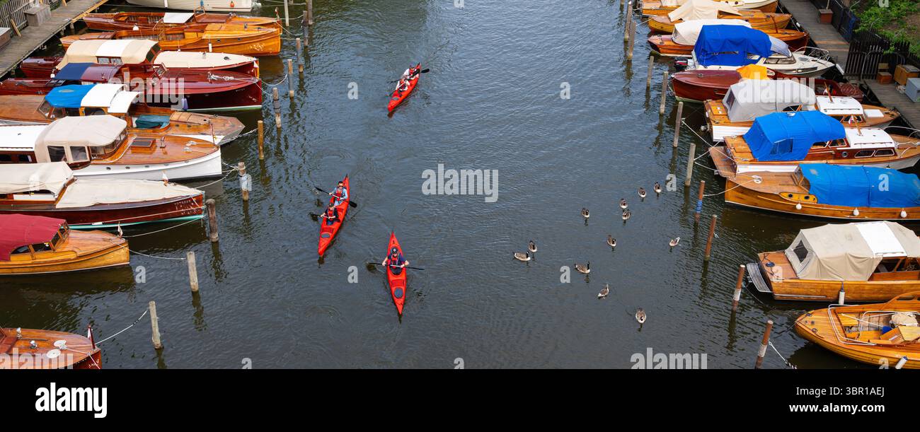 Stoccolma, Svezia - 10 giugno 2025: Veduta aerea di un tranquillo corso d'acqua costeggiato da barche in legno, alcune ricoperte di teloni blu. I kayak navigano attraverso t Foto Stock