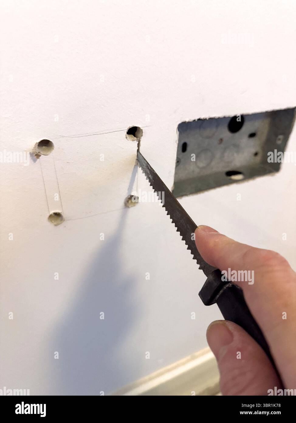Utilizzare una sega per cartongesso per cartongesso per tagliare un foro quadrato in una parete bianca per installare una scatola di presa elettrica o un materasso uk - Immagine stock catturata con smartphone