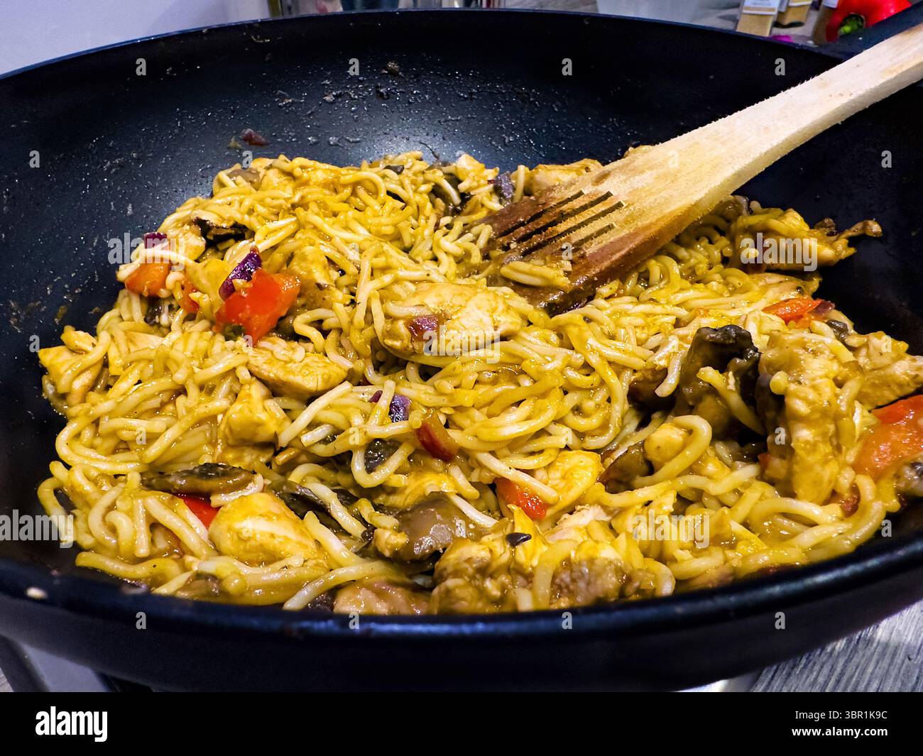 Spaghetti saltati in padella con pollo e verdure cucinati in un wok o in padella con una spatola di legno, mostrando un appetitoso piatto della cucina asiatica Foto Stock