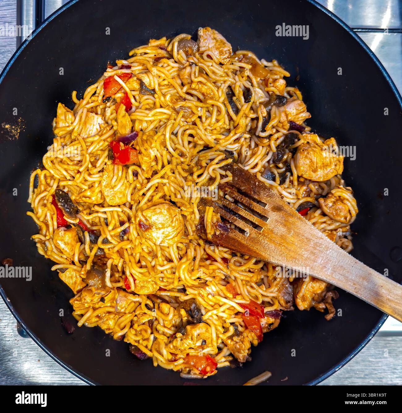 Spaghetti saltati in padella con pollo e verdure cucinati in un wok o in padella con una spatola di legno, mostrando un appetitoso piatto della cucina asiatica Foto Stock