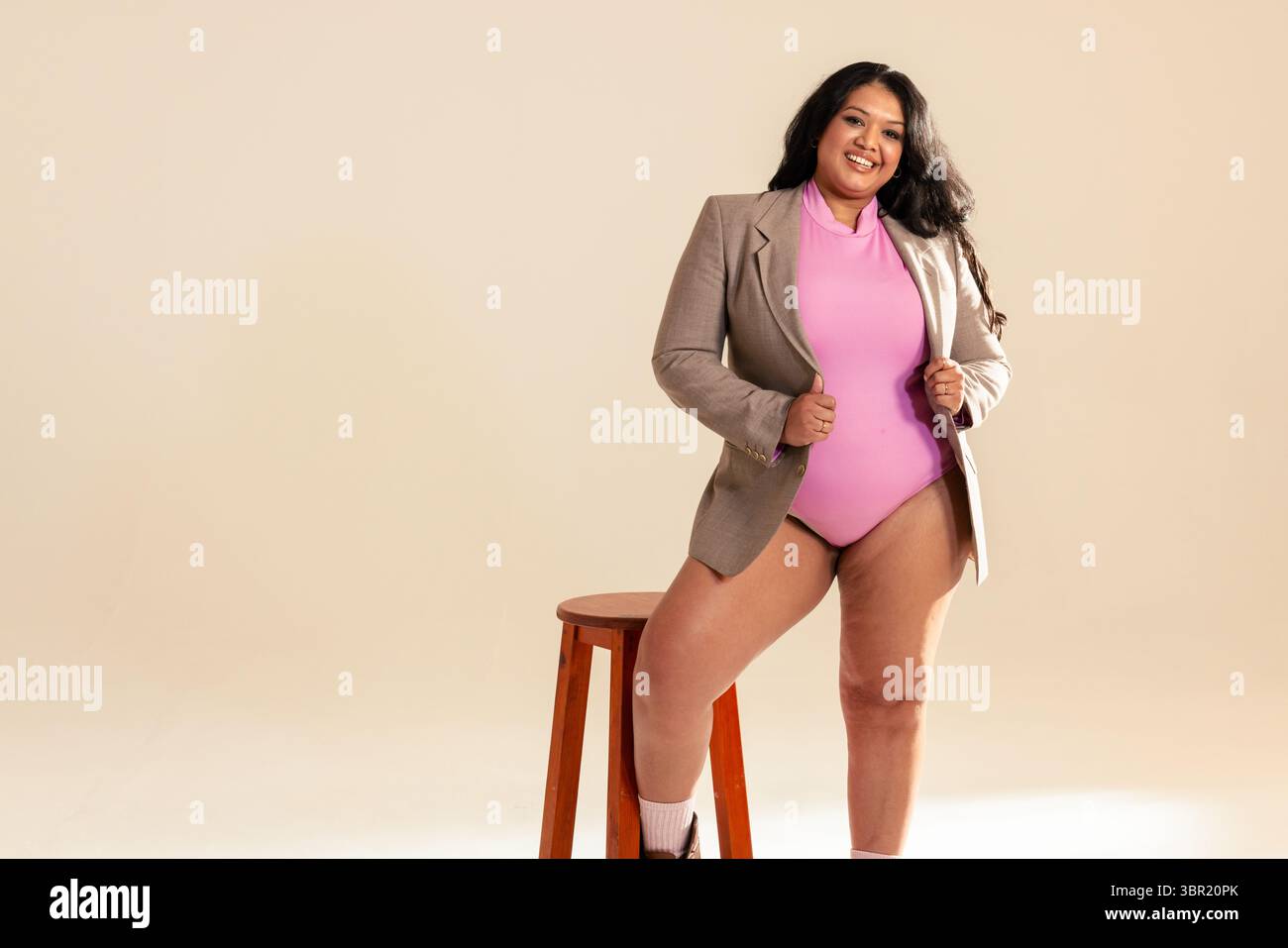 Donna indiana degli anni '30 in piedi in studio con un body rosa che regge revers blazer, copia spazio. Moda, ritratto, minimalista, professionale, bellezza Foto Stock