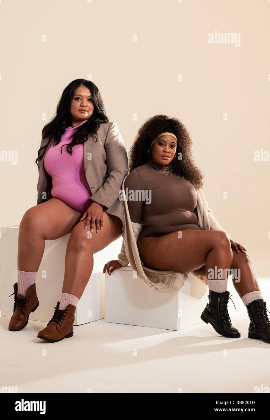 Diverse colleghe di sesso femminile che si pongono su blocchi cubici bianchi in studio e che mettono in mostra le tute. Moda, modellazione, studio, contemporaneo, sicuro di sé, elegante, pr Foto Stock
