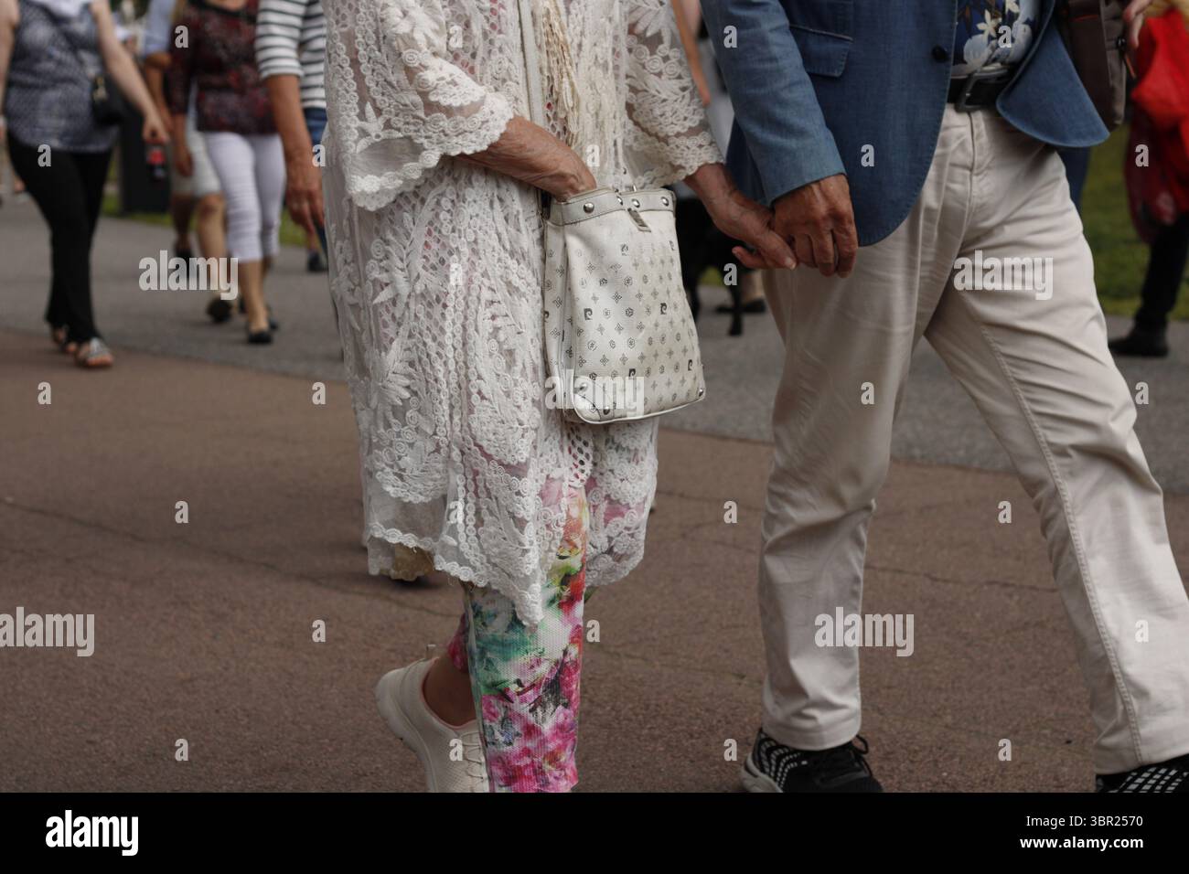 Una foto a livello dell'anca di una coppia anziana che si tiene per mano e cammina durante un evento. Foto Stock