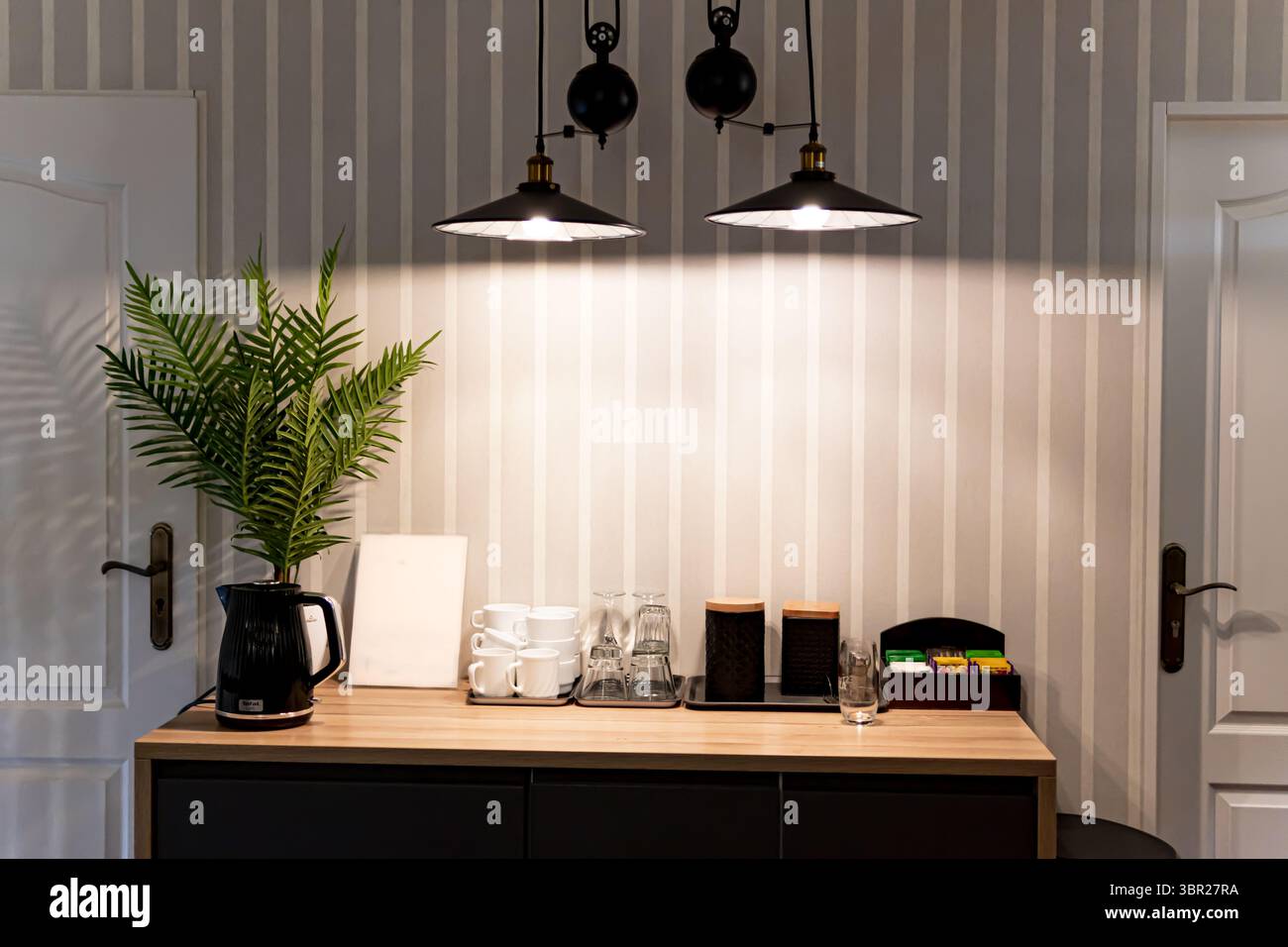 Un tavolo in legno con teiera, tazze e set da tè completo, illuminato da due lampade a sospensione. Foto Stock