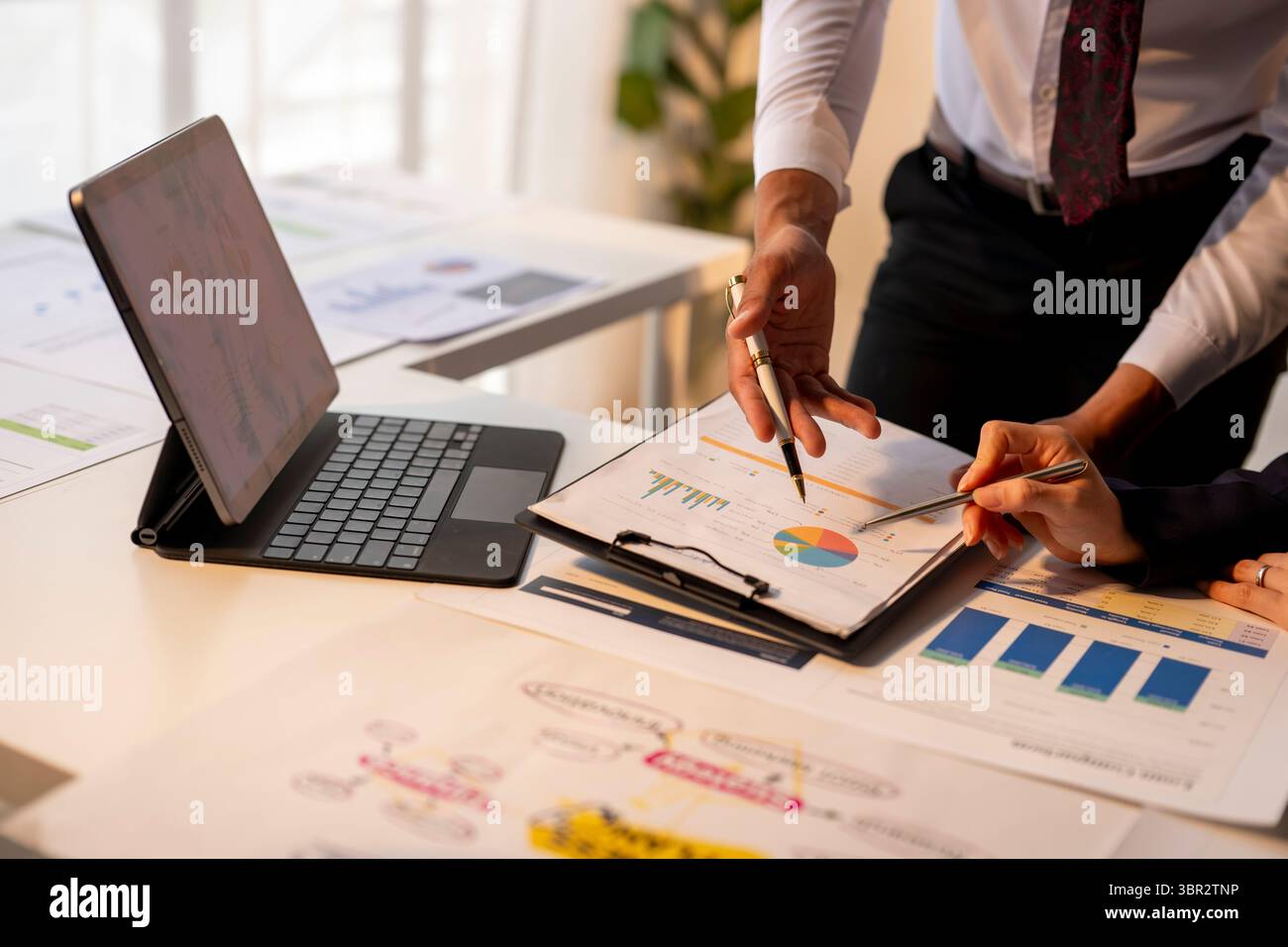 Un uomo e una donna stanno guardando un portatile e un pezzo di carta con sopra dei grafici. Stanno discutendo i dati e prendendo decisioni basate sull'infor Foto Stock