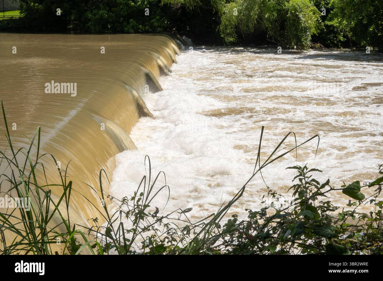 Texas 2025 acque fangose rilasciate dalla diga di controllo delle inondazioni a monte scorre sopra una piccola diga Foto Stock