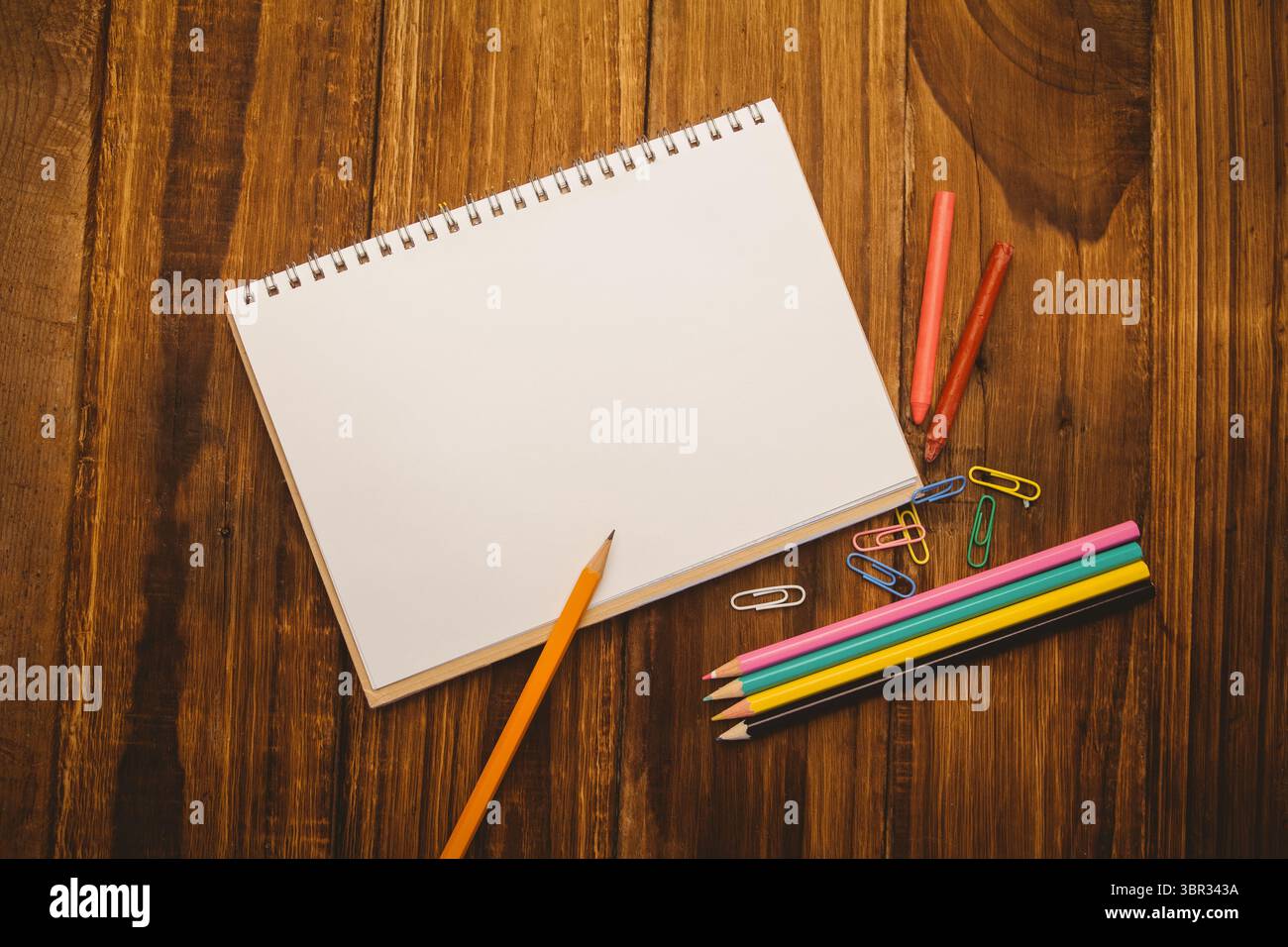 Sketchbook è appoggiato su una scrivania in legno in stile vettoriale piatto con matite colorate, pastelli e graffette Foto Stock