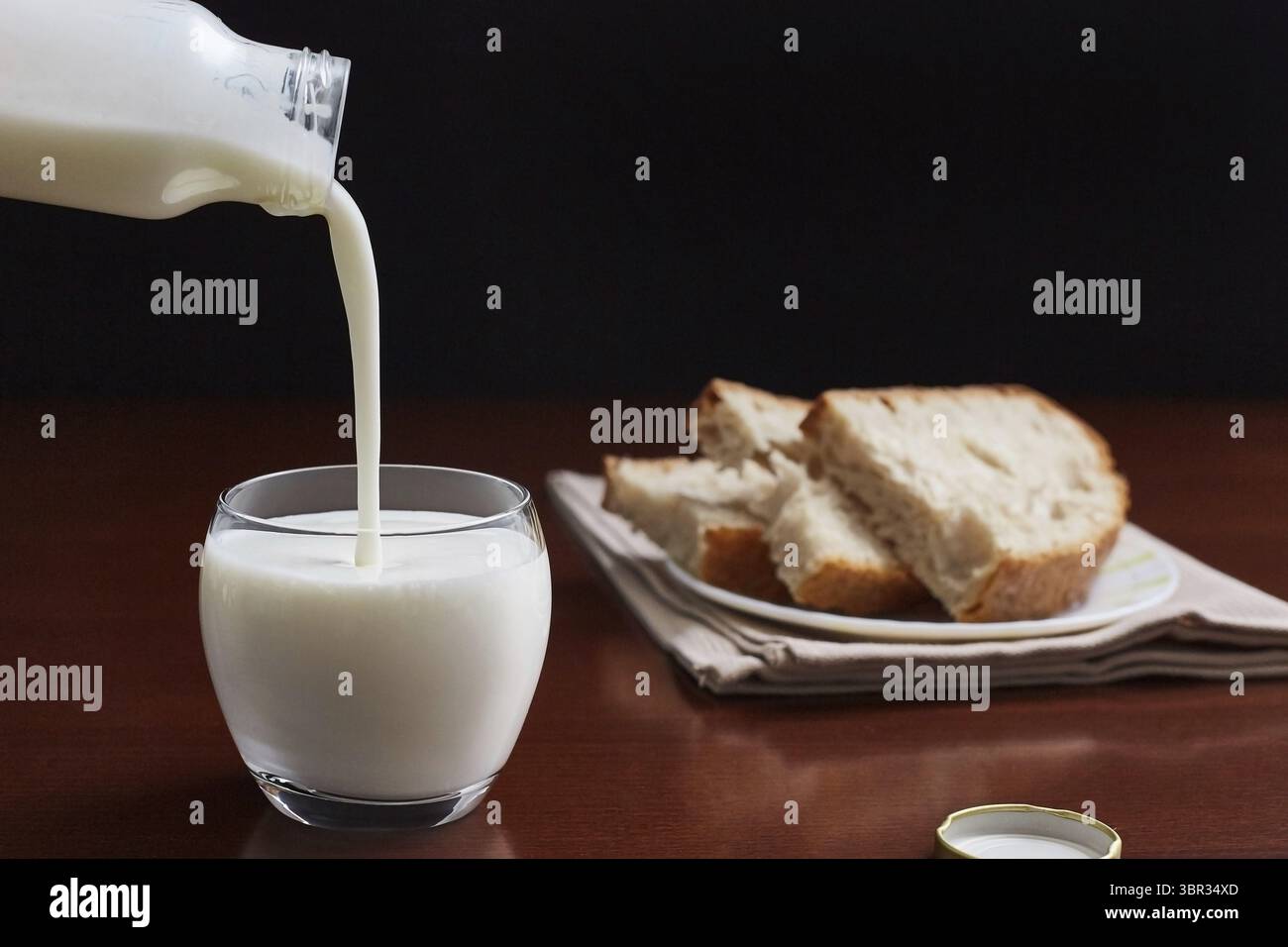 Il kefir sta versando e una piccola bottiglia in una tazza di vetro su un tavolo scuro e sullo sfondo. Pane fatto a mano sullo sfondo Foto Stock Il kefir sta versando e una piccola bottiglia in una tazza di vetro su un tavolo scuro e sullo sfondo. Pane fatto a mano sullo sfondo Foto Stock