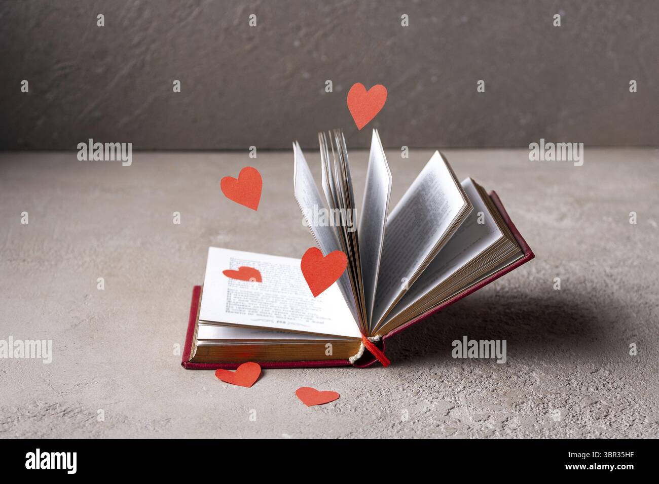 I cuori di carta rossa volano intorno a un libro aperto Foto Stock