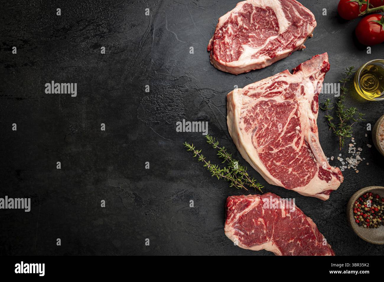 Varietà di bistecche fresche di carne cruda Black Angus prime T-Bone, New York, Ribeye e stagionatura su sfondo nero, vista dall'alto Foto Stock