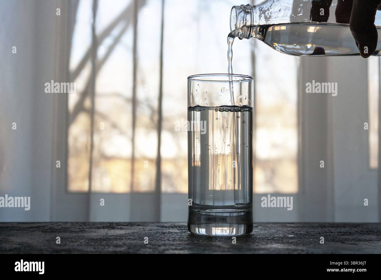 Un vetro trasparente è riempito di acqua da una bottiglia Foto Stock