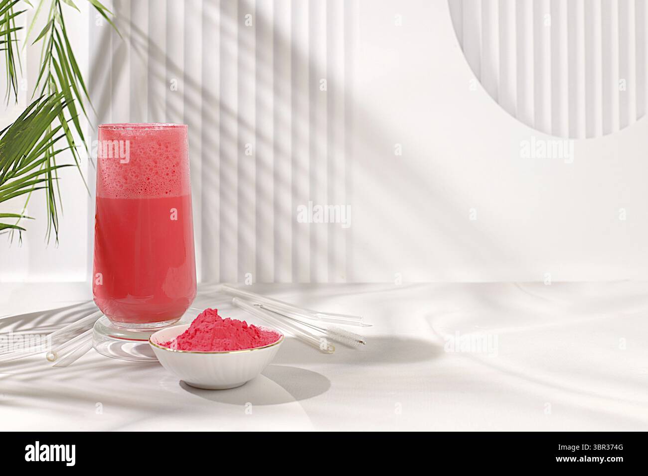 Latte con tè matcha rosa e latte su un elegante sfondo soleggiato della cucina con foglie di palma e polvere di matcha. Bevanda indiana tradizionale ricca di antiossidanti Foto Stock