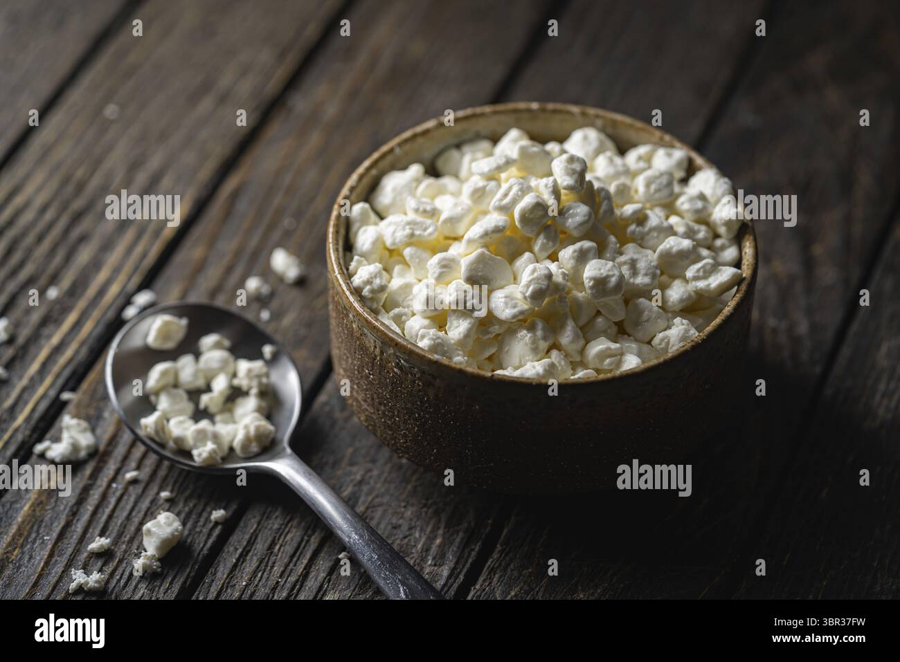 Contadini ricotta formaggio in una ciotola di argilla, accanto ad un cucchiaio su sfondo di legno scuro, Close-up. Naturale cibo sano, sano cibo sano sano sano Foto Stock