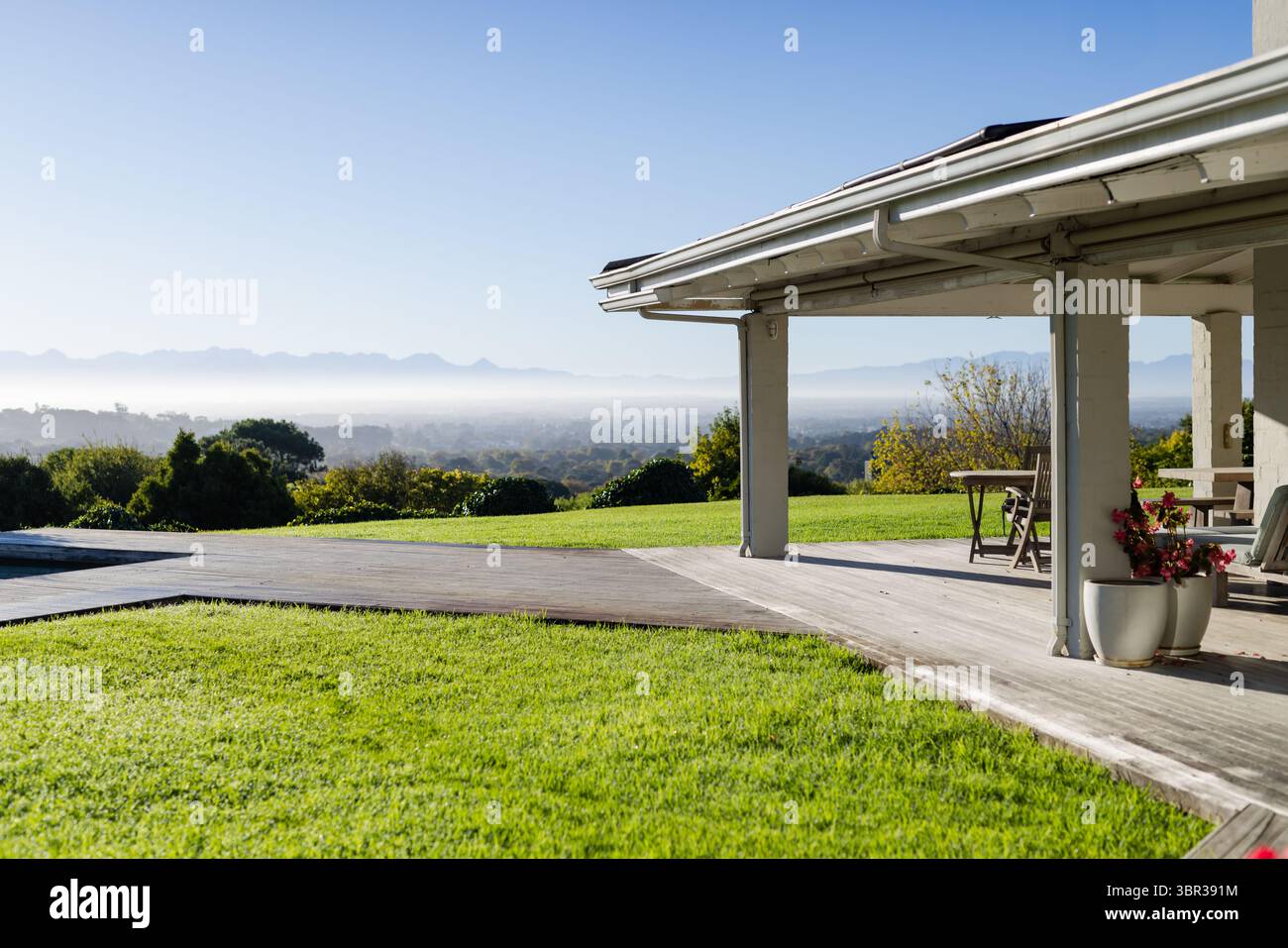 Il tetto del patio sul retro è ombreggiato da un ponte in legno con pilastri, tavolo, sedie, piantatrici e vista sulla valle Foto Stock