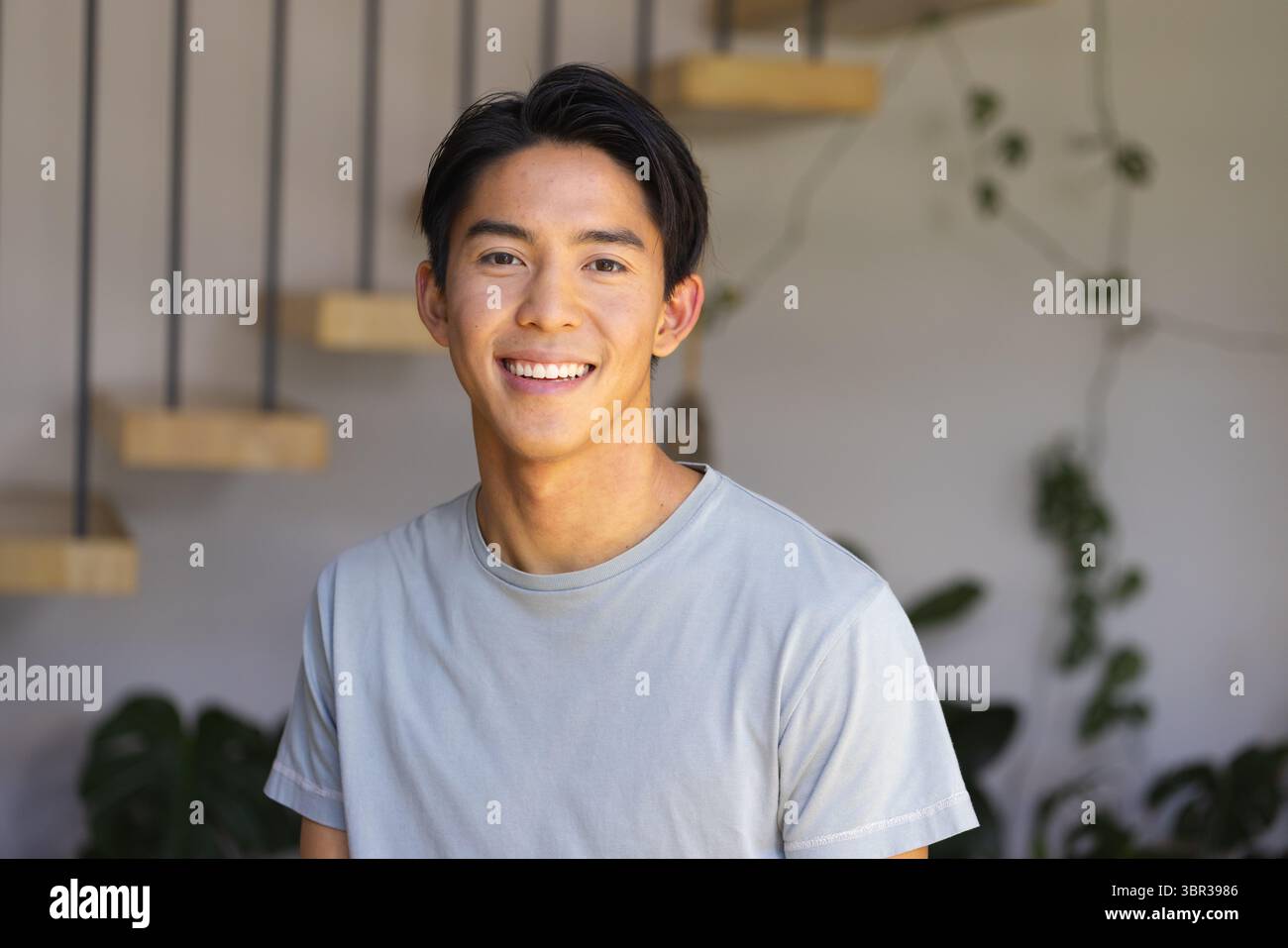 Uomo asiatico in piedi in un ingresso moderno su una scala di legno con vite rampicanti e piante in vaso Foto Stock