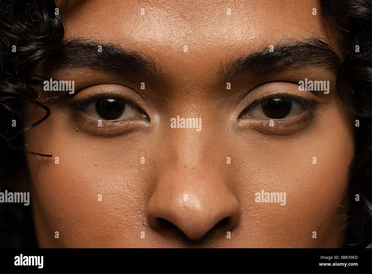 Singolo non binario che guarda dritto in studio con sfondo scuro che si concentra sull'espressione Foto Stock