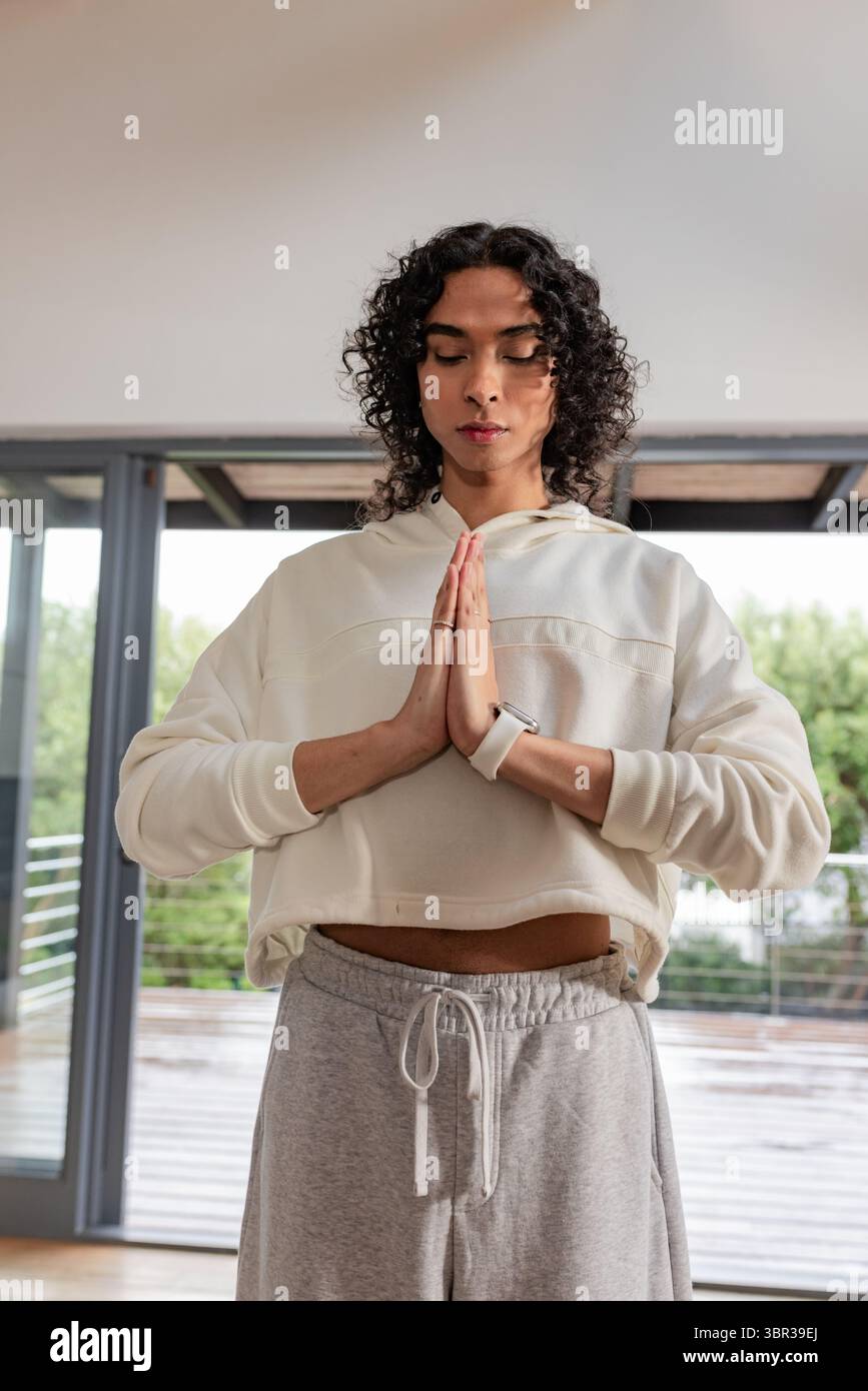Persona non binaria che meditava sul pavimento di casa indossando felpa con cappuccio corto, pantaloni in tuta e smartwatch Foto Stock