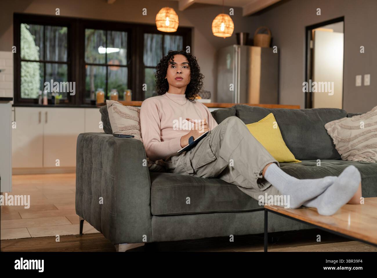 Posto a sedere individuale non binario sul divano con scrittura a cuscino giallo nel notebook nella cucina del soggiorno Foto Stock