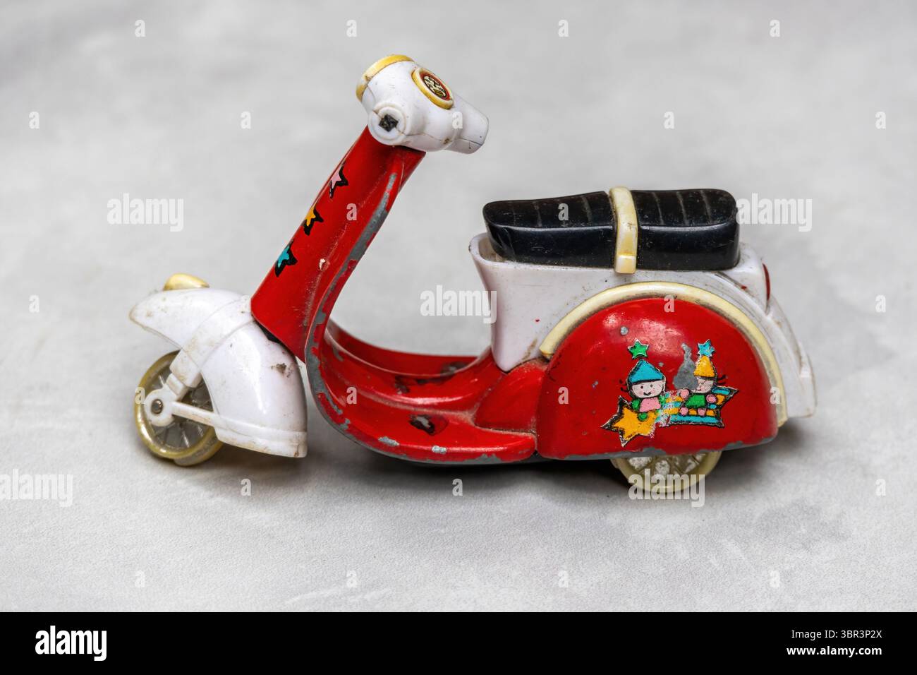 Scooter giocattolo rosso intemprato, visto lateralmente, senza manici e pneumatici. Questo gioco per bambini mostra parti rotte visibili, evocando Foto Stock